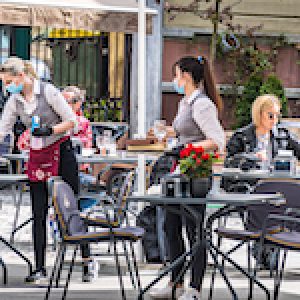 Waitresses with a mask and gloves disinfecting the table of an outdoor bar, caf√© or restaurant with blonde girls at the table