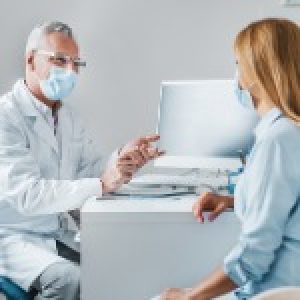 senior-male-doctor-wear-protection-face-mask-talking-with-patient-in-picture-id1266812230