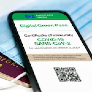The digital green pass of the european union with the QR code on the screen of a mobile phone over a surgical mask and a passport